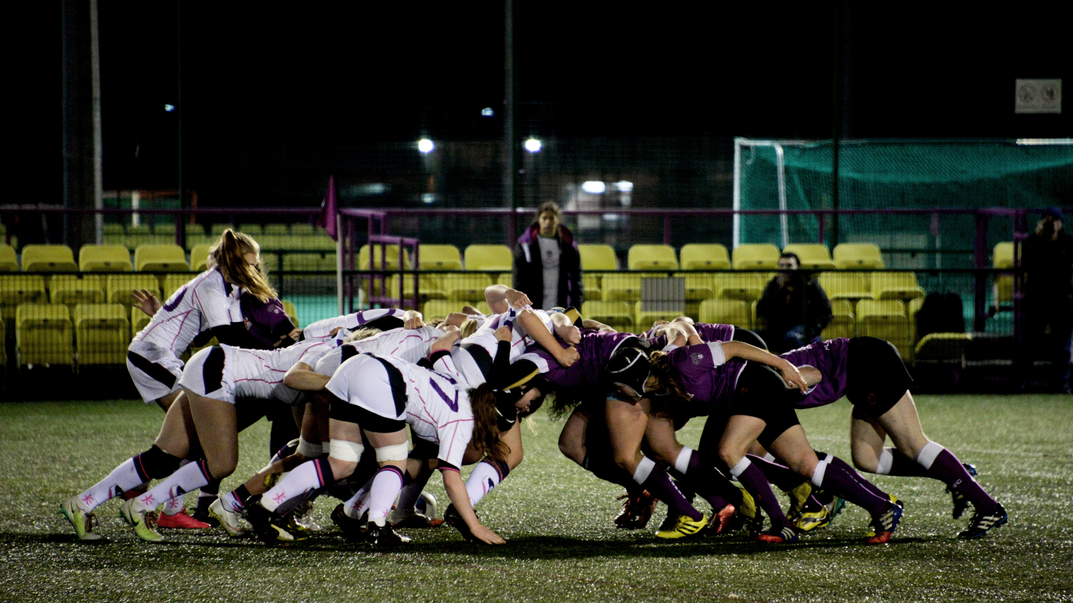 A scrum between two women's rugby teams in white and purple respectively