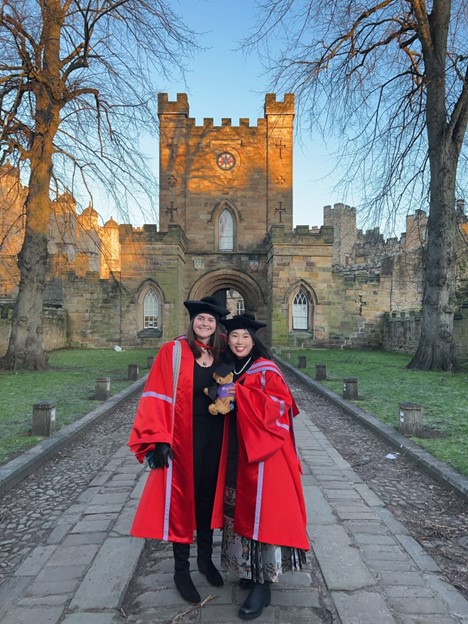 Two PhD Graduates posing outside Durham Castle on Winter Graduation Day.