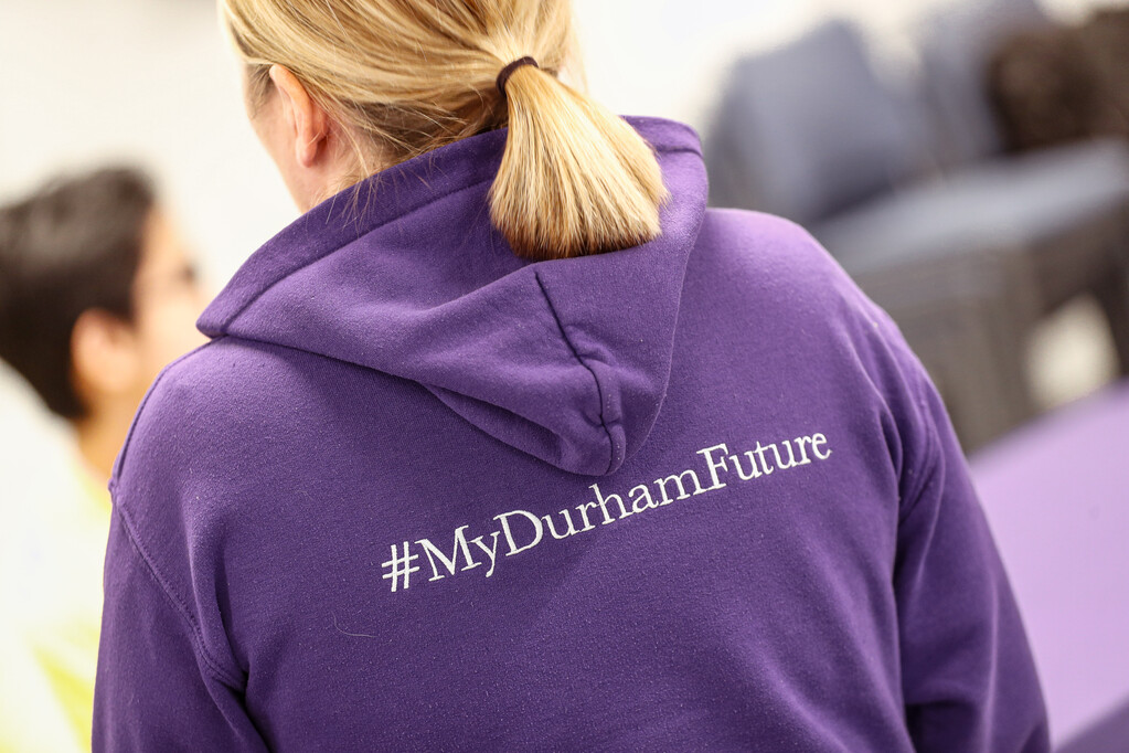 Blonde woman with her back turned showing a purple DU hoodie with #MyDurhamFuture