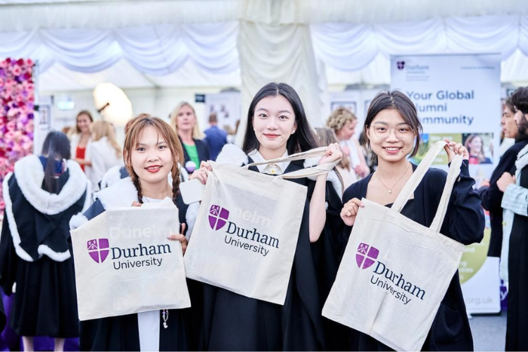 Three students in graduation gowns holding Durham University bags