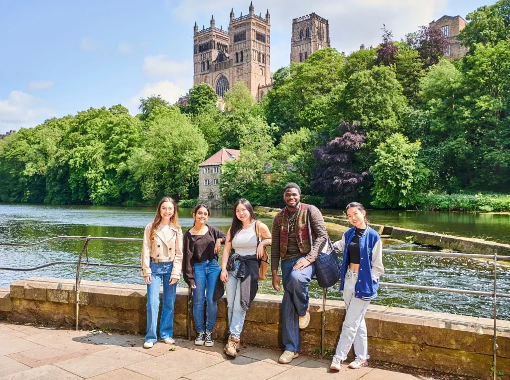 Students standing next to the riverside with the cathedral in the background