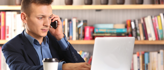 A business student in a library on the phone with a laptop and coffee