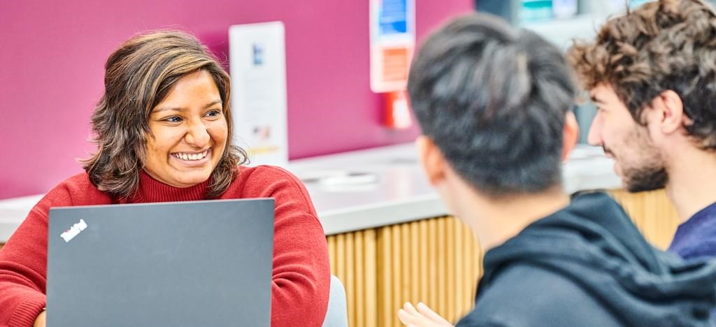 A smiling mature student looks over a laptop at other students