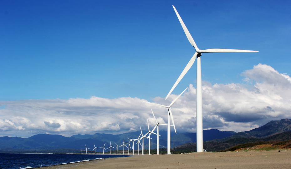 A windfarm located on a beach with mountains in the background