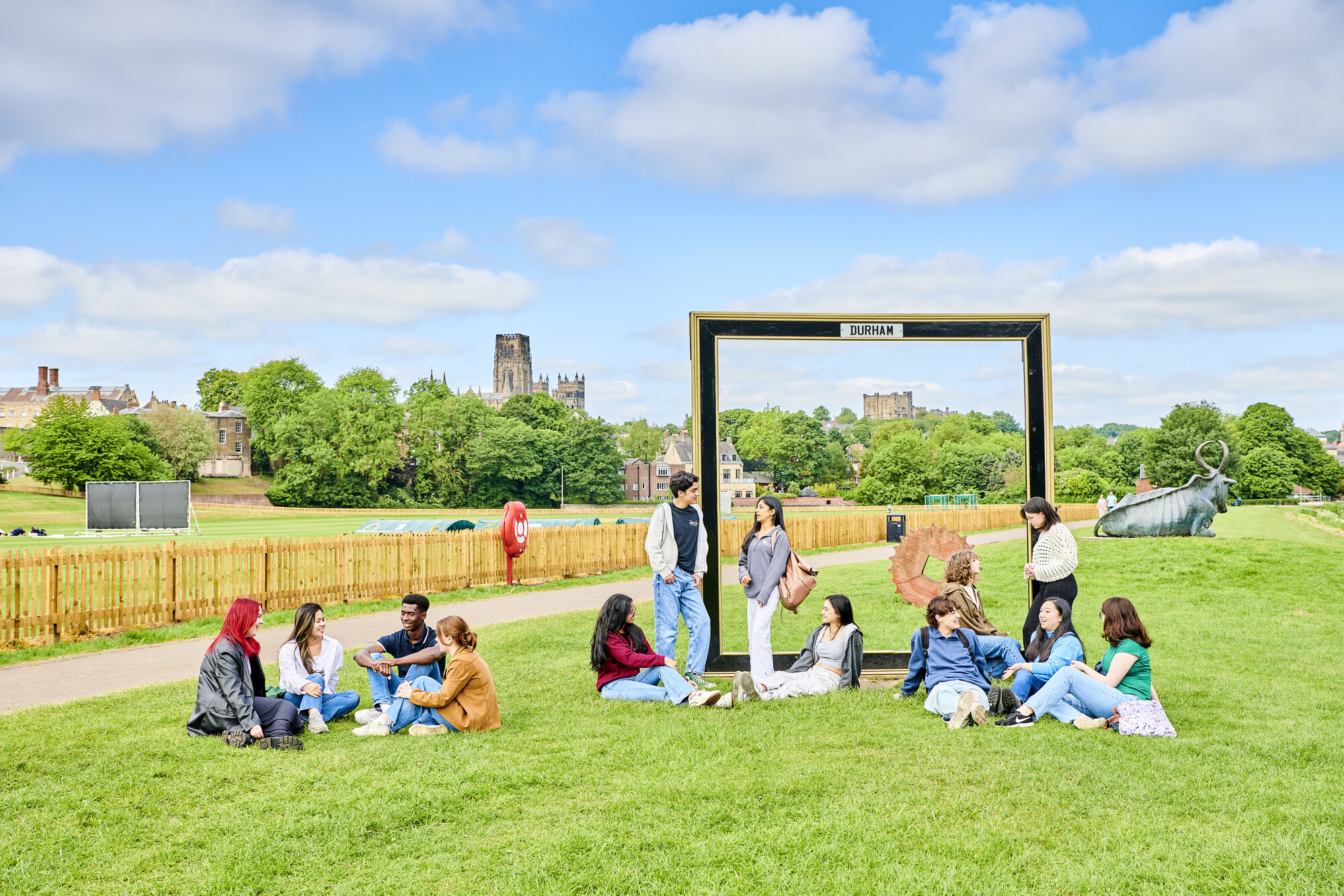 Groups of students sitting and standing on grass with Durham Cathedral in the background