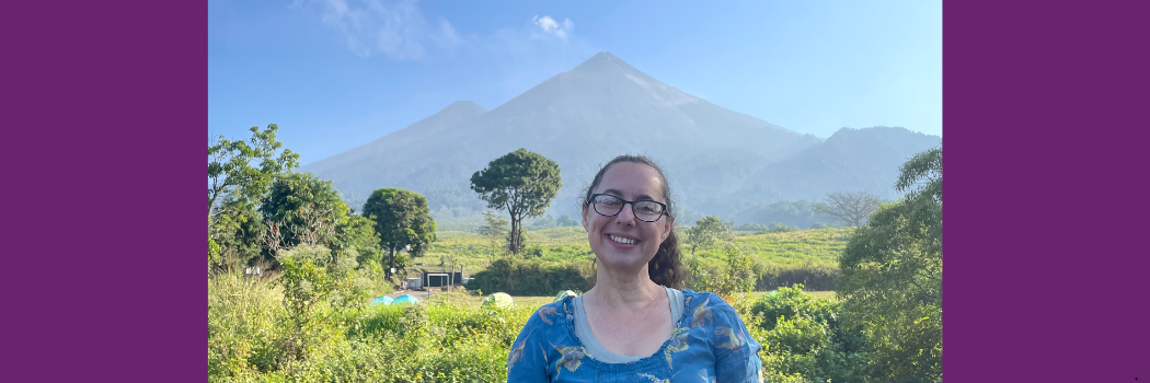 Professor Claire Horwell pictured outside with foliage and a view of a volcano behind her