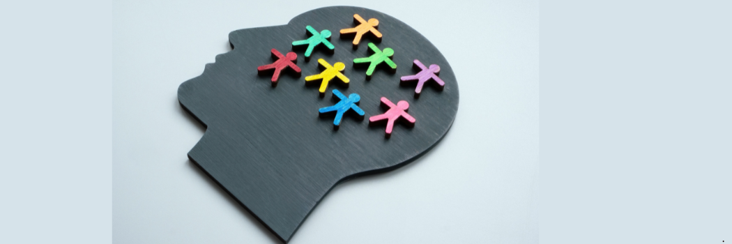Black slate outline of a head on a pale blue background  with small people shaped figurines inside in a range of colours.