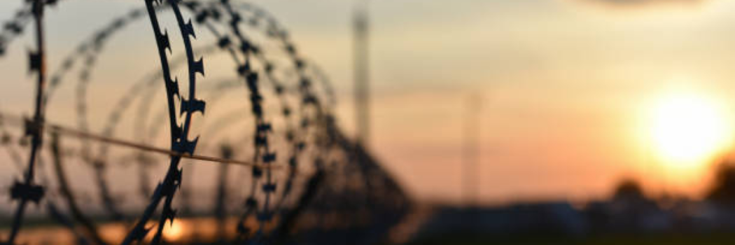 Barbed wire prison fence top against sunset sky