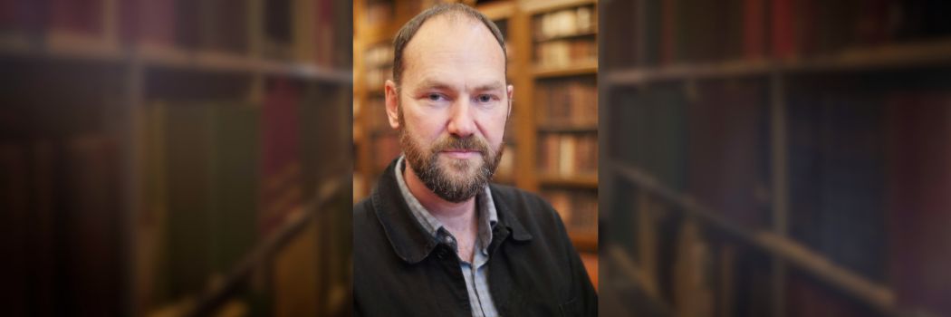 Bearded male in front of old books