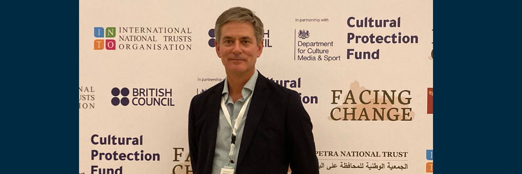 Professor Robin Coningham facing the camera against a backdrop of various names and logos of cultural protection organisations