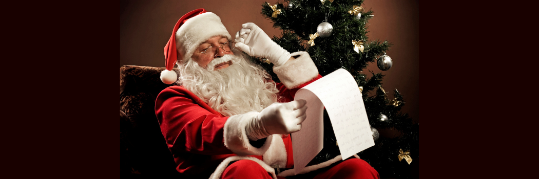 Santa Claus in traditional red clothes and hat holding his glasses to read from a long parchment