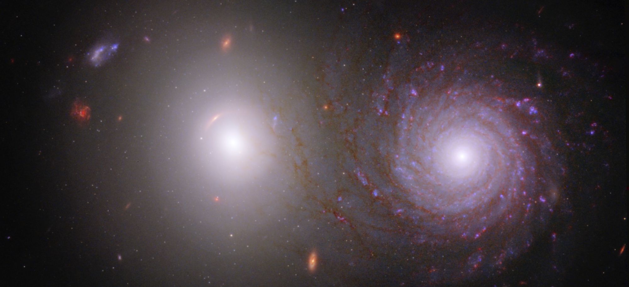 An elliptical and spiral galaxy sit side by side against a backdrop of space and stars