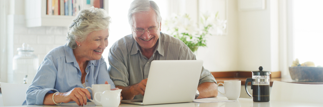 An older couple smiling as they look at a laptop screen on a kitchen surface