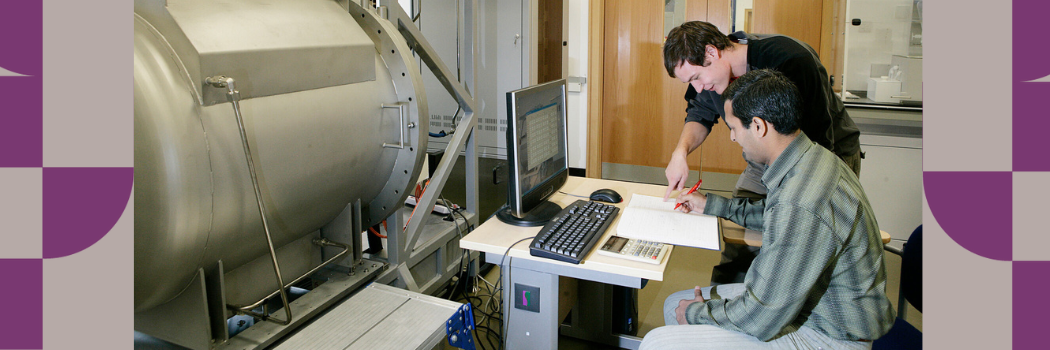 Two male researchers working at a computer with machinery in front of them