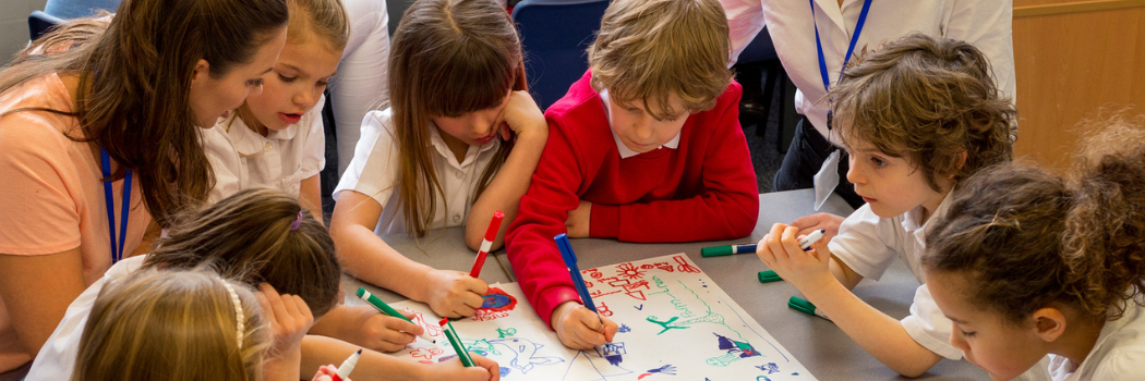 A group of school children draw on a piece of paper in a classroom