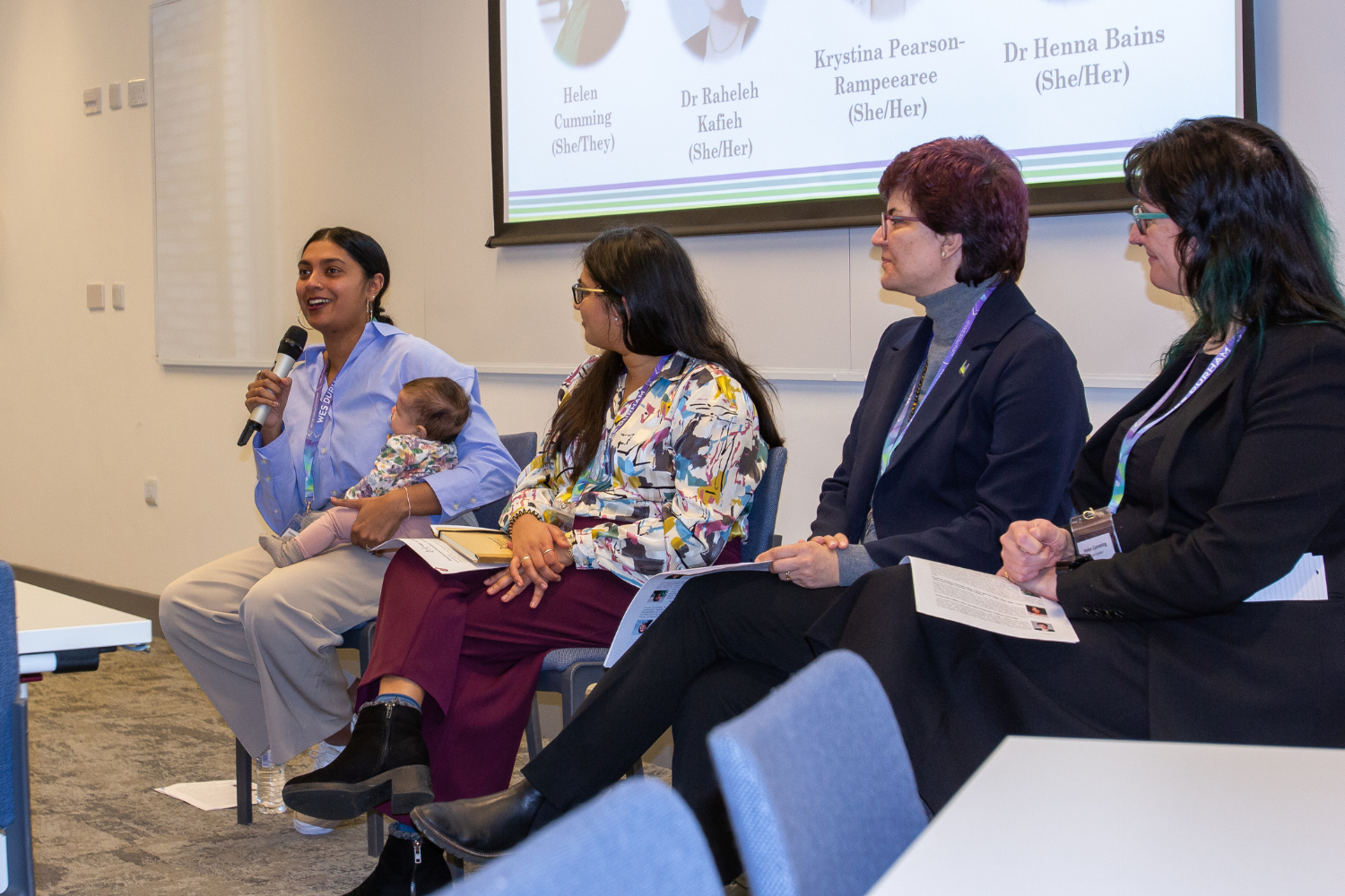 Four women in engineering, one holding microphone and cradling baby, sitting on a panel discussing engineering