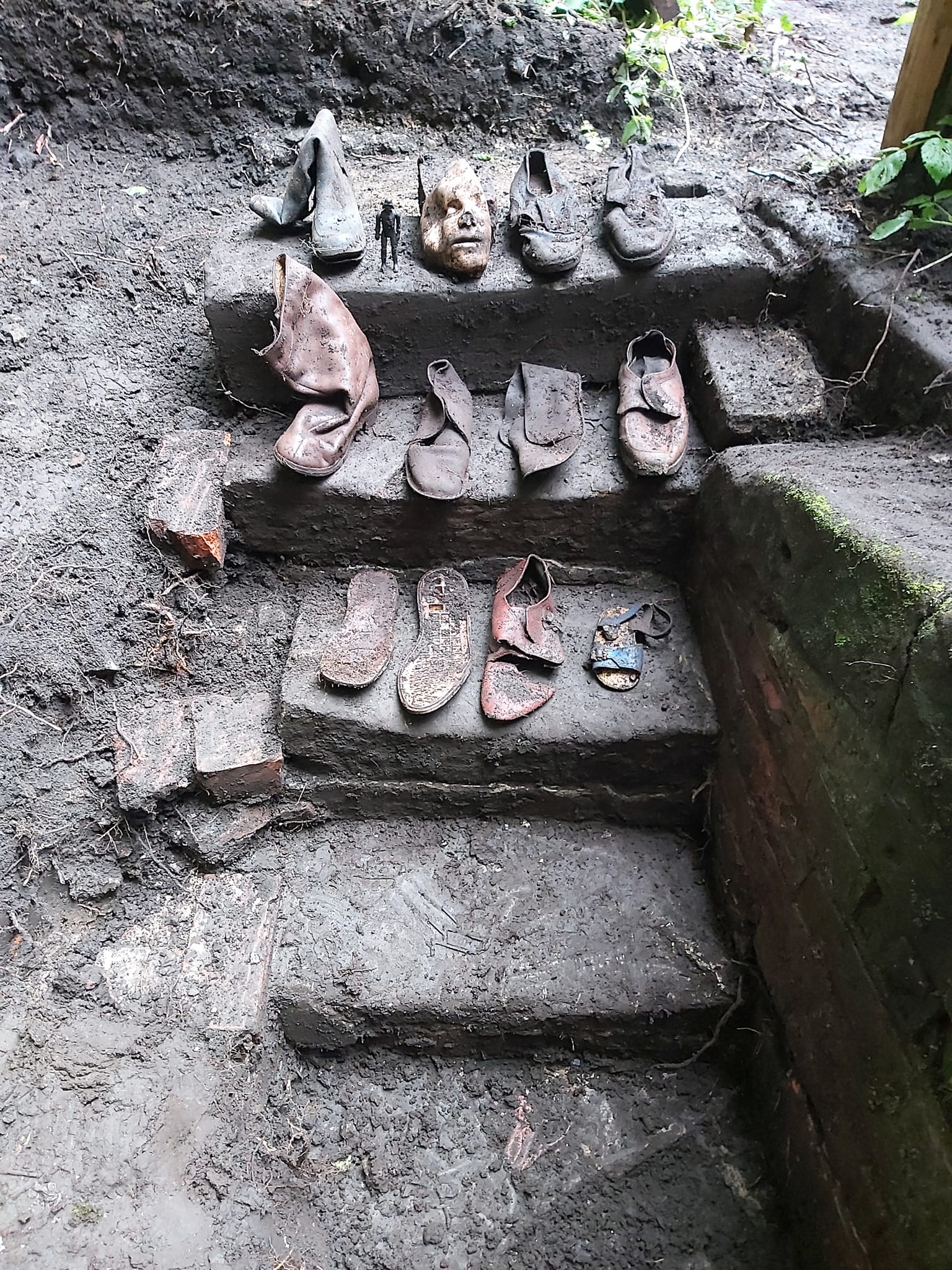 Remains of twelve shoes and a small action figure arranged on some worn stone steps.