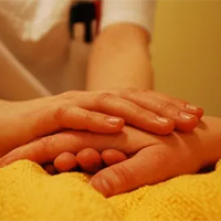 Carer holding hand of patient in bed