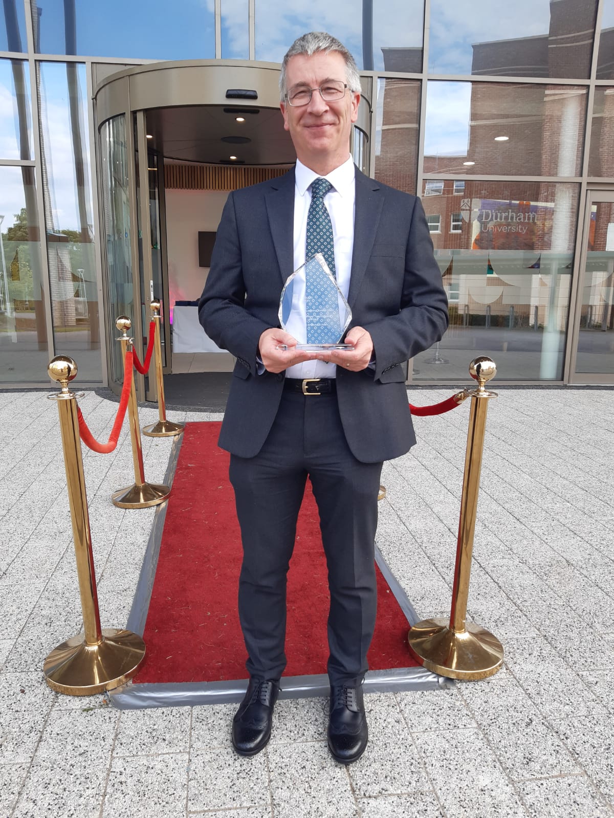 A man standing at the end of a red carpet holding his award