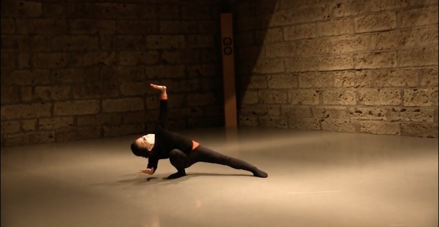 A woman dances in an otherwise empty room with brick walls