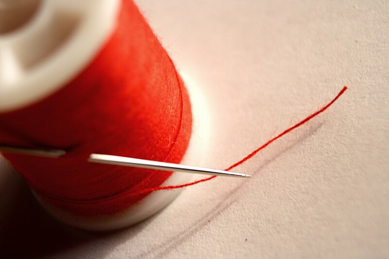 A bobbin of red thread with a needle threaded through it