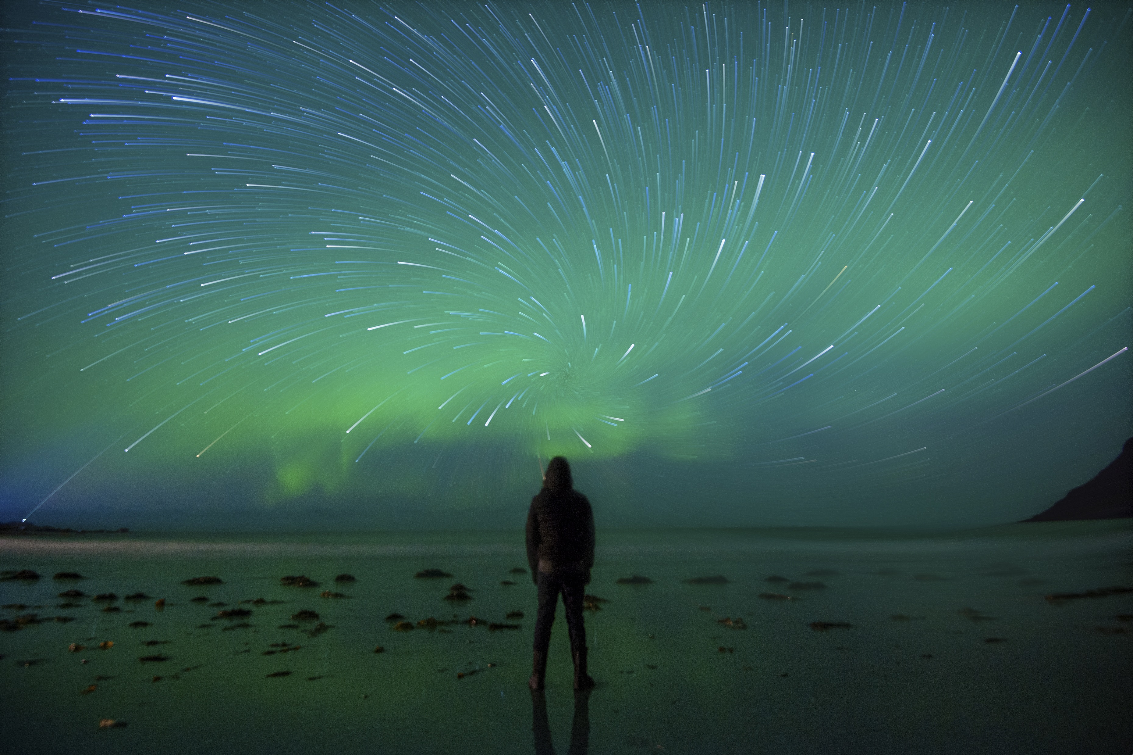 stock photo of person on beach looking up at northern lights