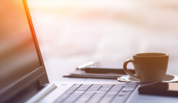 A laptop resting on a table, with a cup of tea beside it.