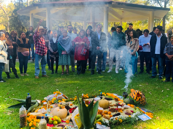 A circle of farmers, academics, and researchers look at a group of colourful items offered to Mother Earth as part of a food sovereignty festival in Mexico, including seeds, fruits, flowers, and books