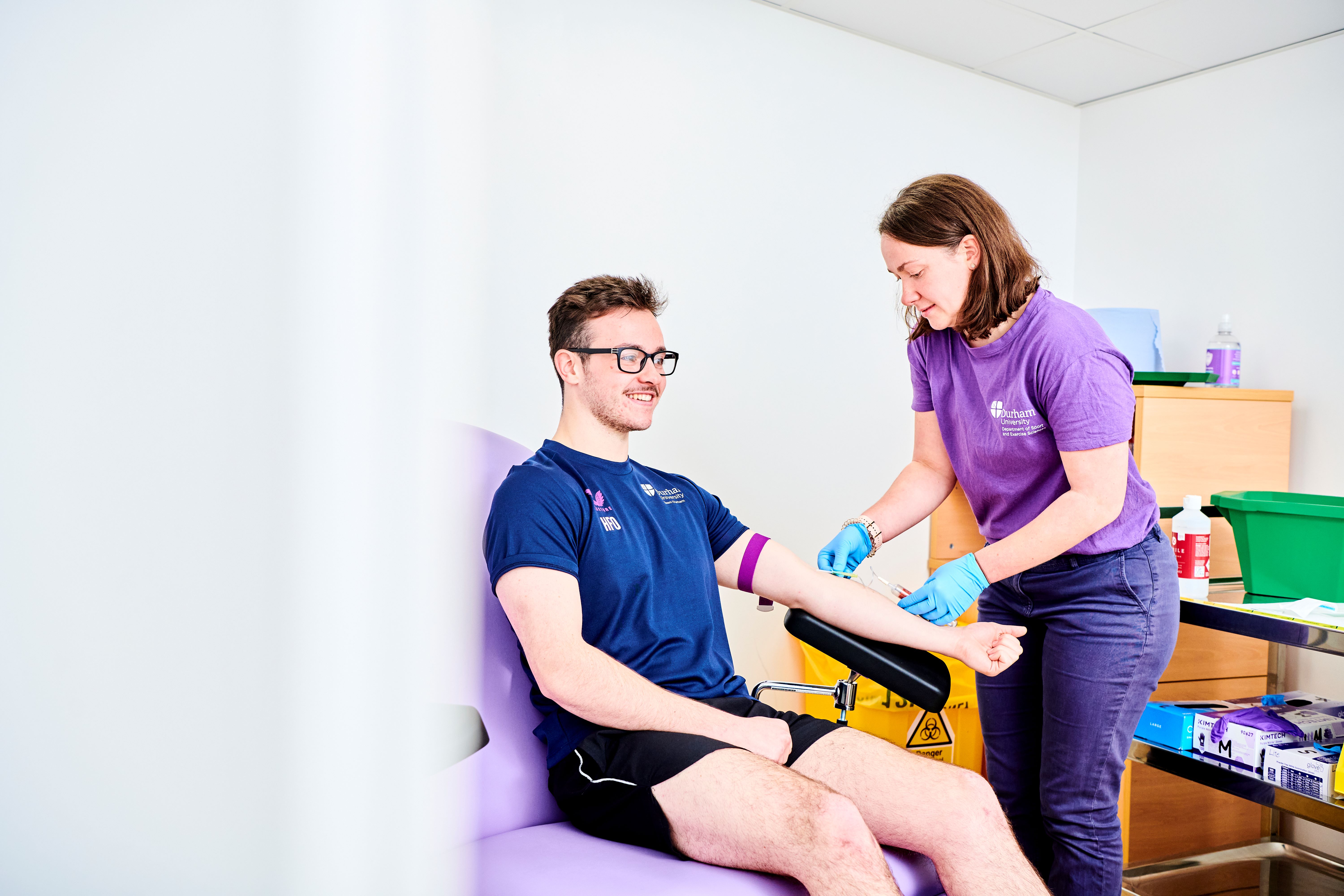 A student sitting in a phlebotomy chair having their blood taken for analysis by staff member