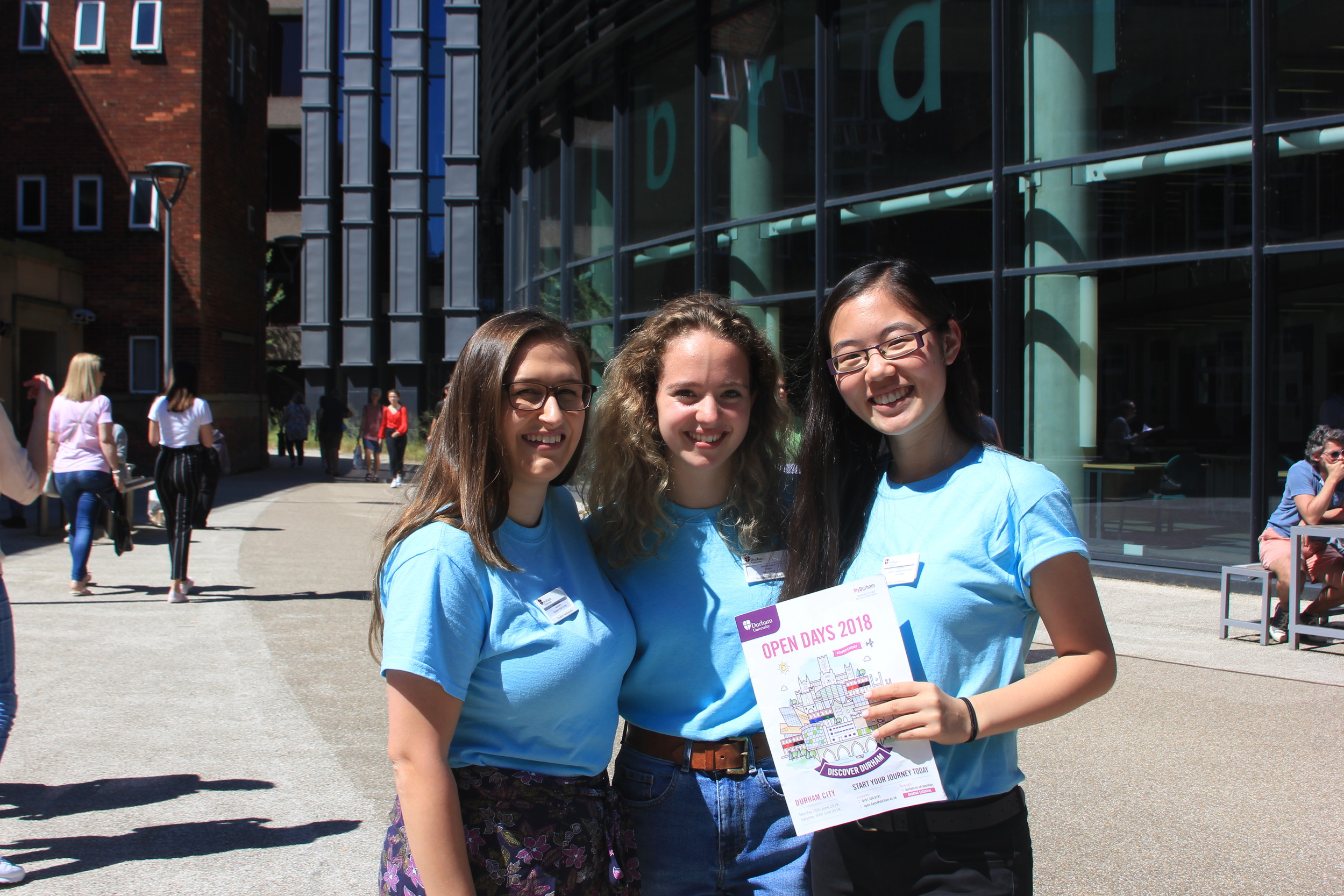 Three students posing and holding an open day brochure