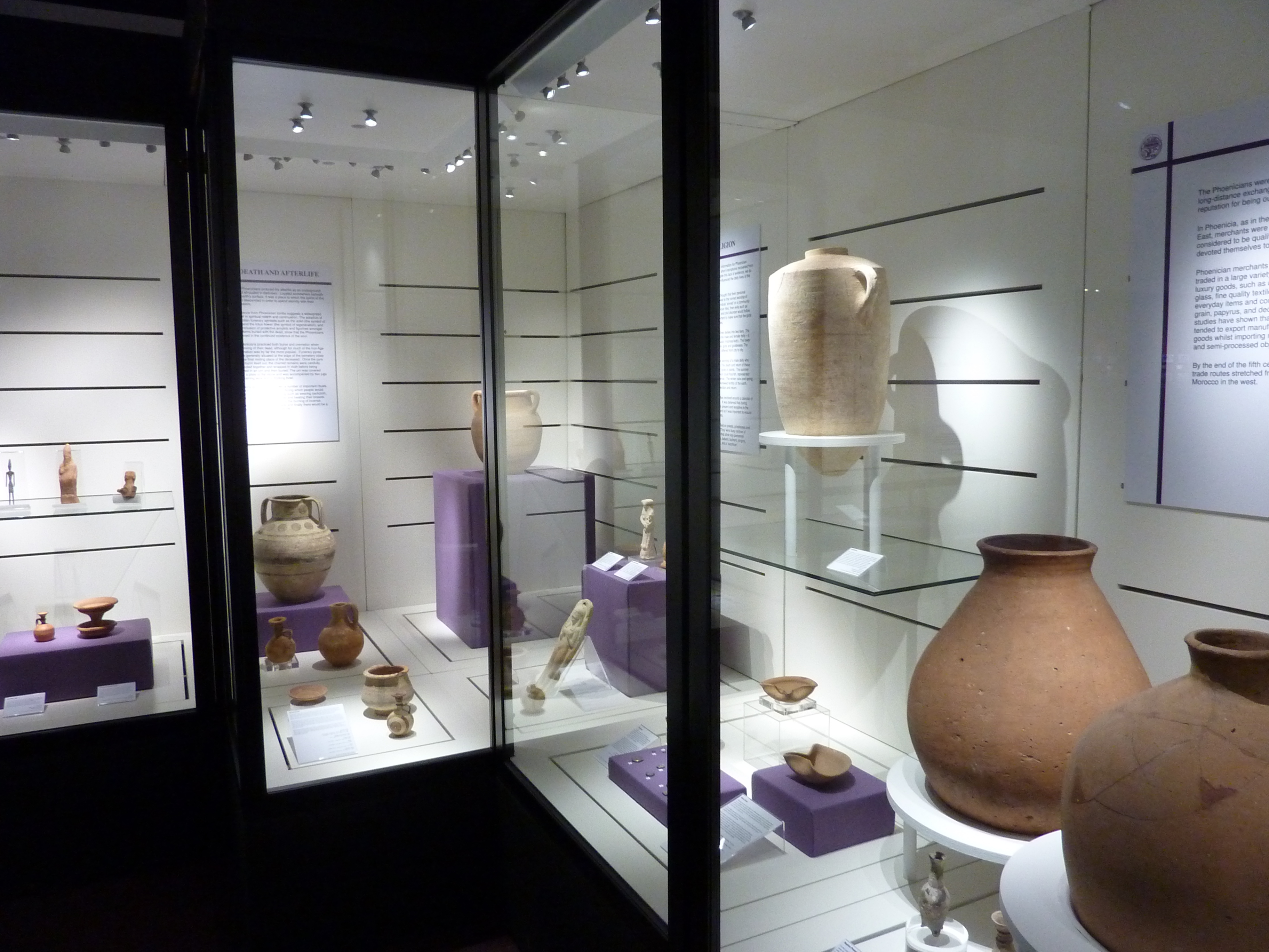 Museum display cases with a range of ancient pottery vessels, small pottery figures and coins at different heights on plinths