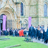 Students in gowns walking along the path to Durham Cathedrals North Door