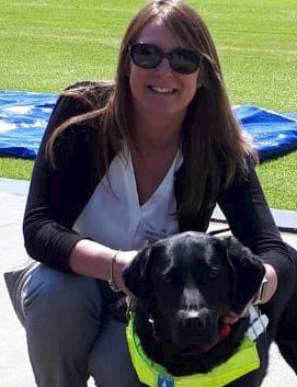 Headshot of Angela Johnson, she is light skinned, wearing sunglasses and a dark cardigan, and is with her guide dog Nutmeg, a black Labrador.