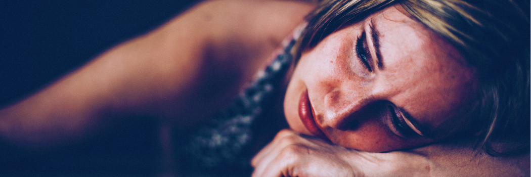 A sad woman lies on the floor with her fist under her face.