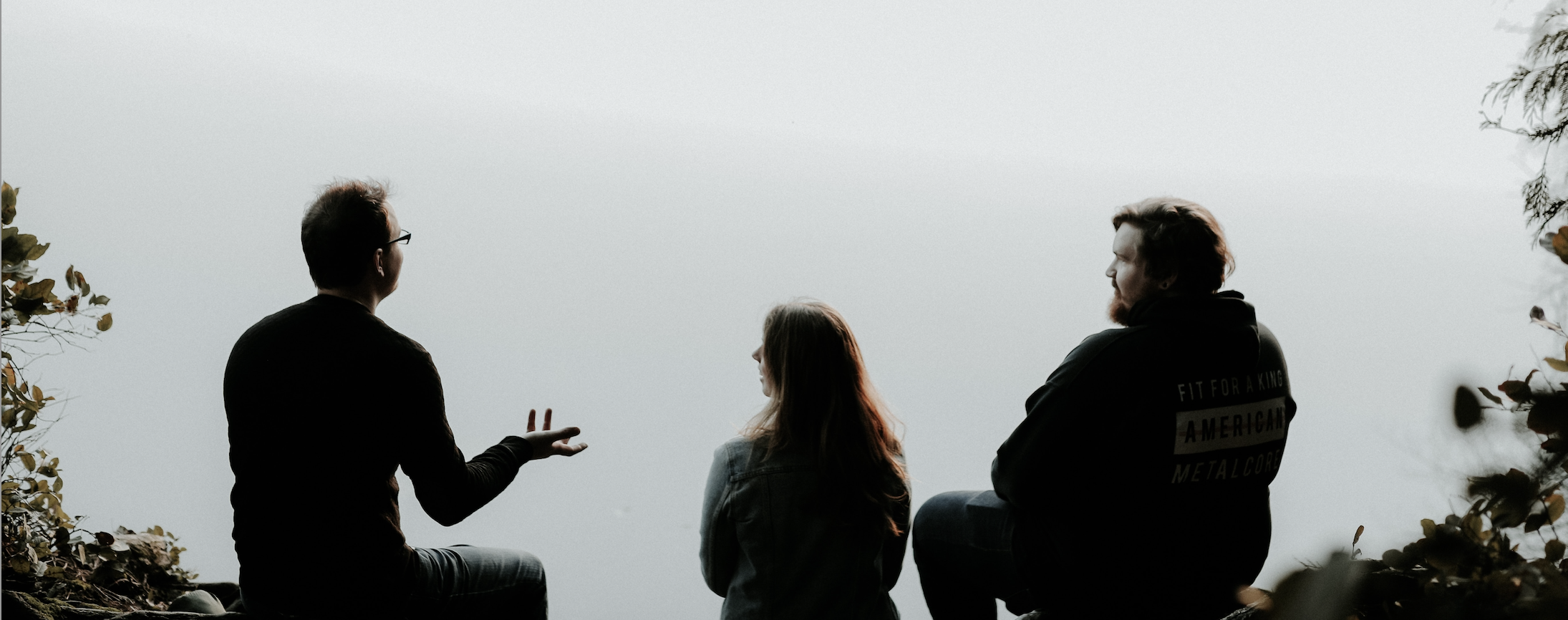 A silhouette of three people sitting on a cliff in foggy weather