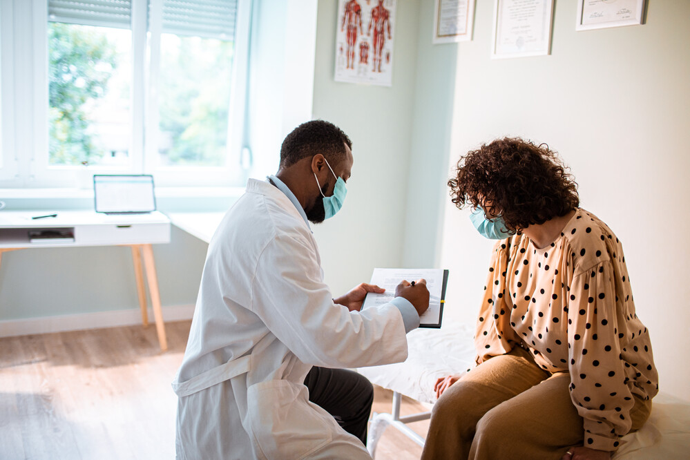 Doctor in a medical mask showing a chart to a patient, also in a medical mask