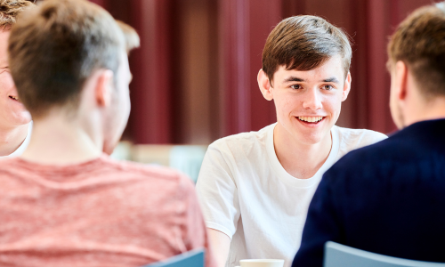 A male student chatting with two other males with their back to us