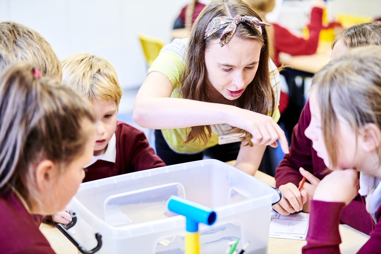 Children sitting at a table looking into a plastic tub